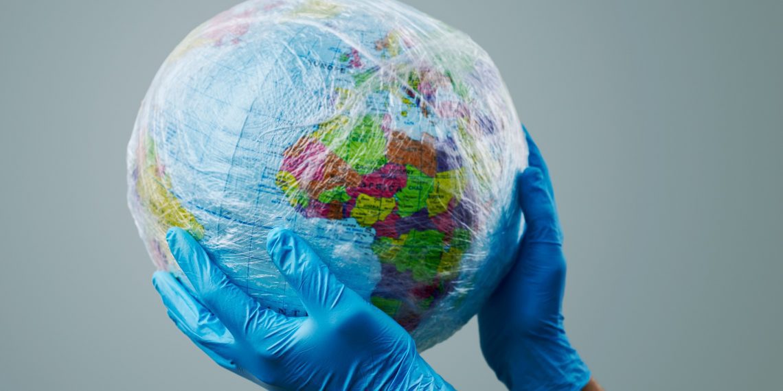 a doctor man wearing blue surgical gloves holding a world globe wrapped in plastic, depicting the plastic contamination or the protection against the epidemic infectious diseases or the air pollution